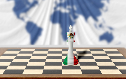 Mexican chess king covered with country flag is on a wooden chess board on table against world map background. Easy to crop for all your social media and design need with copy space.