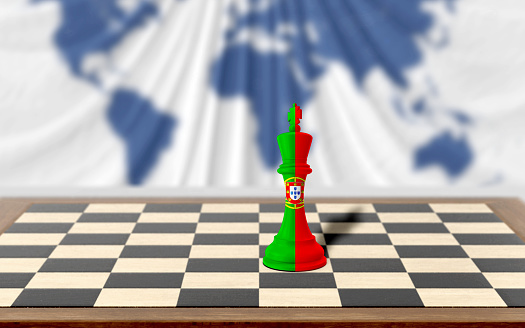 Portuguese chess king covered with country flag is on a wooden chess board on table against world map background. Easy to crop for all your social media and design need with copy space.