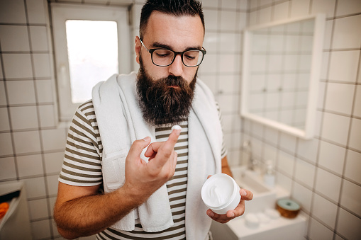 Man applying face cream on his face in bathroom