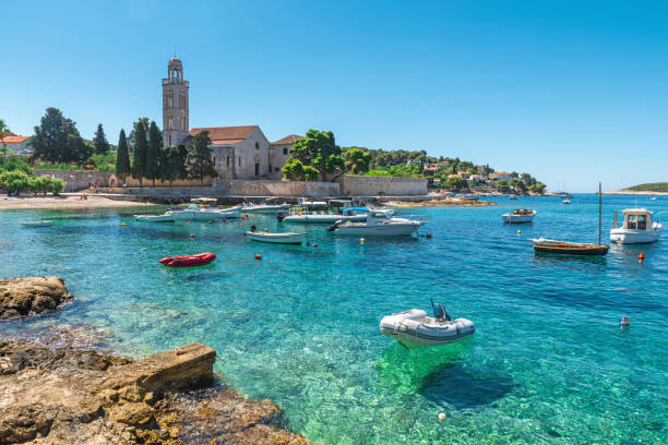 acqua turchese della baia del mare adriatico sull'isola di hvar con monastero francisciano e barche nella regione della dalmazia, croazia - croatia foto e immagini stock