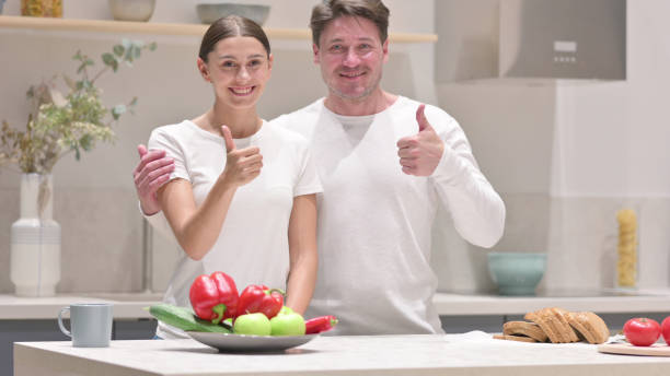 casal mestiço mostrando polegares para cima sinal na cozinha - 5412 - fotografias e filmes do acervo