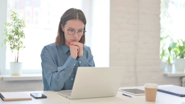 istock Young Woman with Laptop Thinking at Work 1331795177