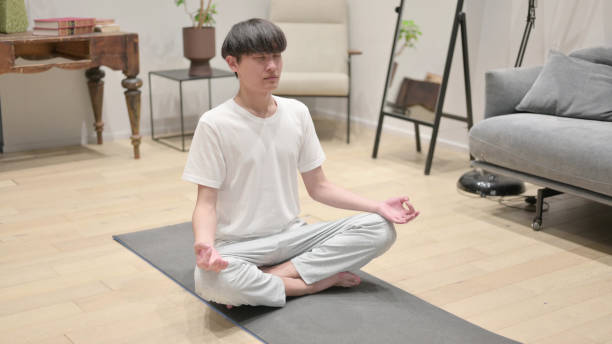 giovane uomo asiatico che medita sul tappetino yoga a casa - 5552 foto e immagini stock