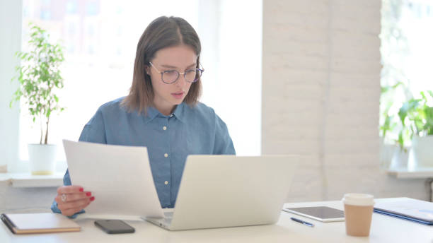 istock Young Woman with Laptop Reading Documents in Office 1331795319