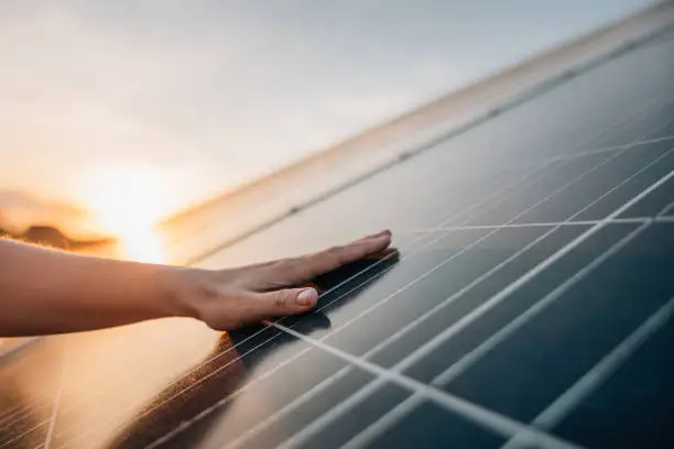 Close-up of human hand touching solar panel during Sunset