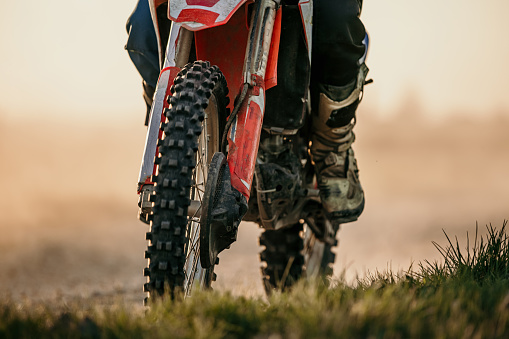 Low Section of motocross rider riding dirt bike through grass field