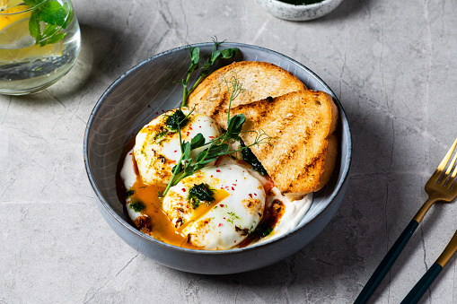 Cilbir or Turkish Eggs. poached eggs topped over herbed greek yogurt, drizzled with hot spiced paprika olive oil. Turkish breakfast in a grey bowl on marble background. shakshuka with pepper