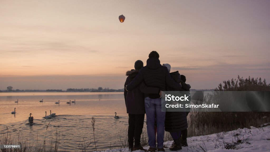 Family admiring sky lantern from riverbank Family in warm clothing admiring sky lantern in air from riverbank Family Stock Photo