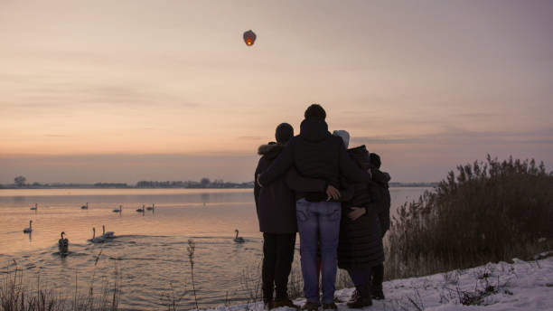 family admiring sky lantern from riverbank - balloon child winter snow imagens e fotografias de stock