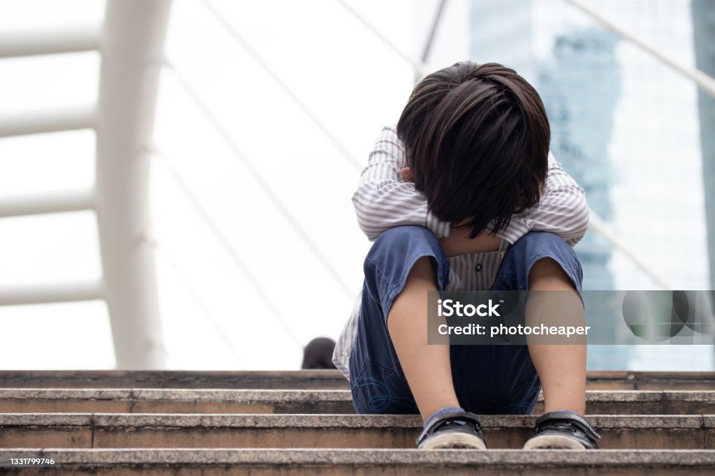 Homeless Asian child sitting alone on the stairway in the street. Poor, sad, scared and alone. Child Stock Photo