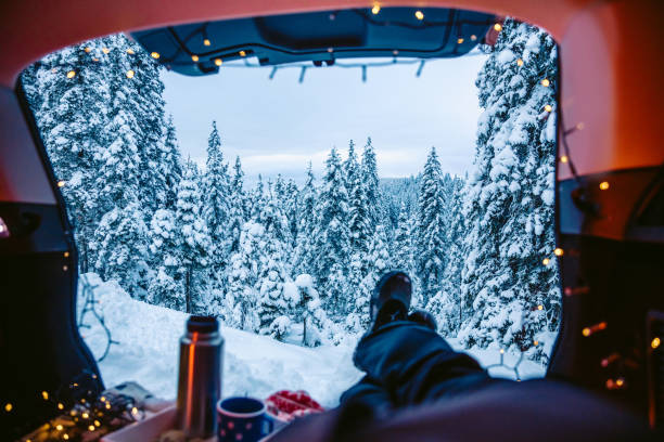 Man resting in car trunk with legs crossed in snow covered forest