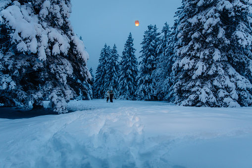 Couple standing on snow covered forest with sky lantern flying in the sky at night