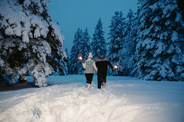 Couple walking while holding sparkler on snow covered forest