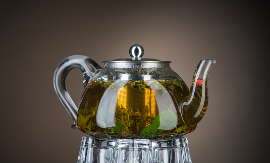 Tea with mint and herbs in a transparent teapot on a brown background. Isolated with backlight