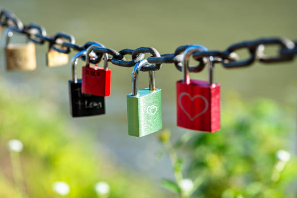 Green padlock suspended on a chain engraved with two hearts.