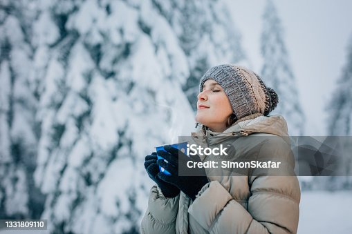 istock Young woman standing on snow covered forest with eyes closed 1331809110