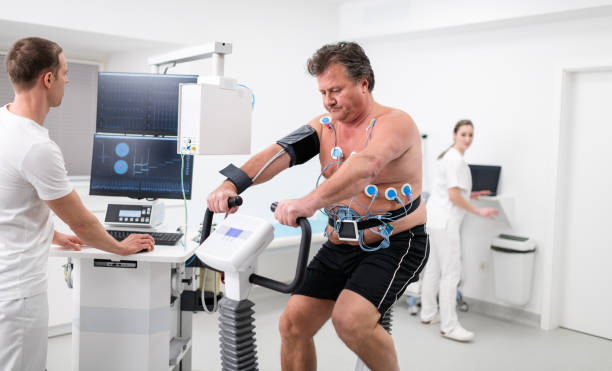 Male Patient Taking A Cardiopulmonary Stress Test In Clinic Doctor observing the progress of a cardiopulmonary stress test taken by the male patient riding a bicycle ergometer. Healthcare and medicine concept. stress test stock pictures, royalty-free photos & images