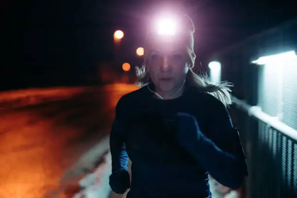 Woman with headlamp listening music and jogging on street at night