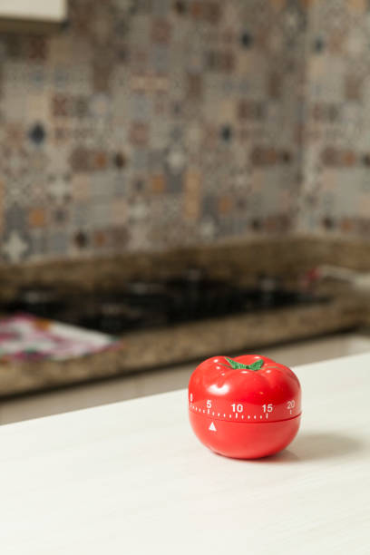 istock Red tomato-shaped kitchen timer with cooking in the background. 1331816437