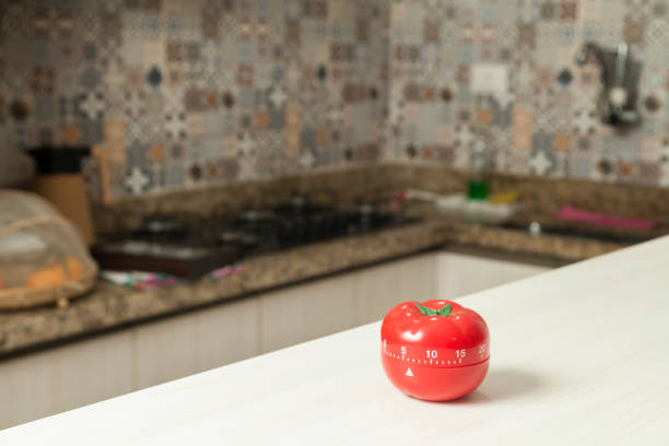 istock Red tomato-shaped kitchen timer with cooking in the background. 1331816438