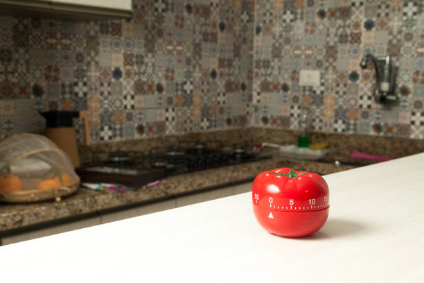 istock Red tomato-shaped kitchen timer with cooking in the background. 1331816444