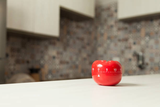 istock Red tomato-shaped kitchen timer with cooking in the background. 1331816460