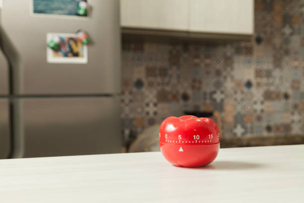 istock Red tomato-shaped kitchen timer with cooking in the background. 1331816519