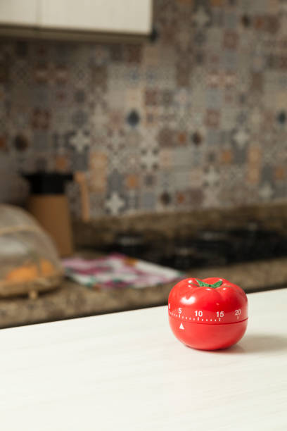 istock Red tomato-shaped kitchen timer with cooking in the background. 1331816534