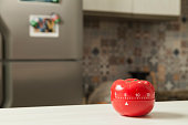 Red tomato-shaped kitchen timer with cooking in the background.