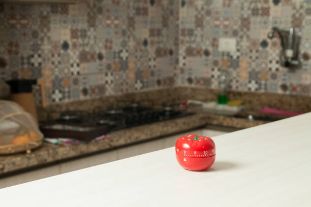 istock Red tomato-shaped kitchen timer with cooking in the background. 1331816545