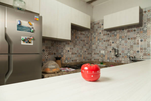 istock Red tomato-shaped kitchen timer with cooking in the background. 1331816572
