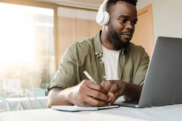 Young african man using computer laptop while wearing headphones at bar restaurant - Conference video call lifestyle technology concept - Focus on face