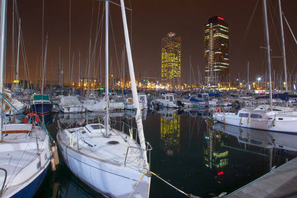Night view of Port Olimpic harbor and marina in Olympic village(Vila Olimpica) in Barcelona. Mooring yachts, boats and other vessels sway at the pier. A summer vacation in Spain at Mediterranean sea. vista nocturna del puerto de port olimpic y el puerto deportivo en la villa olímpica (vila olimpica) en barcelona. yates de amarre, barcos y otras embarcaciones se balancean en el muelle. unas vacaciones de verano en españa en el mar mediterráneo.