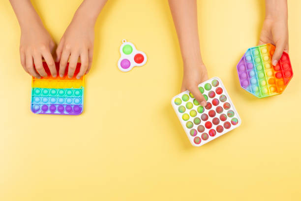 istock Many hands holding pop it fidget toys on yellow background. Push pop-it fidgeting game helps relieve stress, anxiety 1331826896