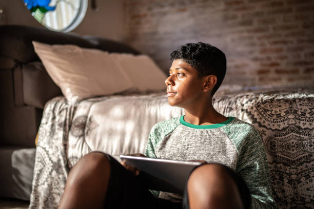 Teenager boy using digital tablet and contemplating at home