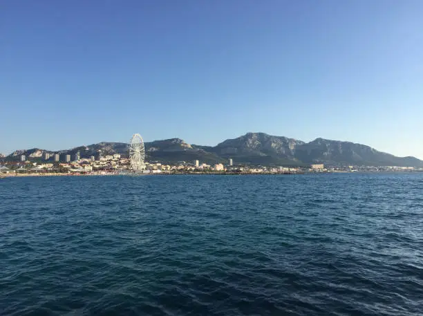 Photo of The Marseilleveyre massif and the Grande Roue de Marseille Ferris wheel seen from the Prado Beach in Marseille, France.