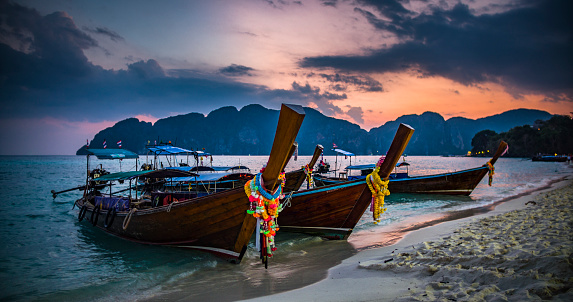 Thai traditional wooden longtail boats moored on a tropical beach in southern Thailand. Beautiful sunset clouds over the Andaman Sea