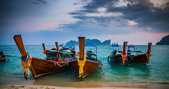 Thai traditional wooden longtail boats moored on a tropical beach in southern Thailand. Beautiful sunset clouds over the Andaman Sea.