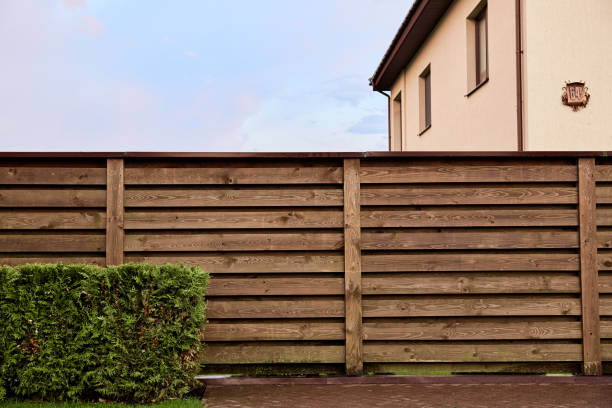 Side view of two-story private country house with wooden fence made of horizontal planks. Number 64. Landscape design. Trimmed green hedge bushes. Copy space. Outside territory. Neighbor separation. vista lateral de la casa de campo privada de dos pisos con cerca de madera hecha de tablones horizontales. número 64. diseño paisajístico. arbustos de setos verdes recortados. espacio de copia. fuera del territorio. separación de vecinos