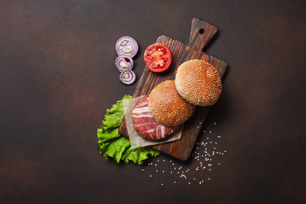 istock Hamburger ingredients raw cutlet, tomatos, lettuce, bun, cheese, cucumbers and onion on rusty background 1331831542