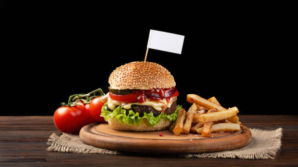 домашний гамбургер крупным планом с говядиной, помидорами, листьями салата, сыром и картофелем фри на разделочной доске. маленький белый фл - burger gourmet hamburger steak стоковые фото и изображения
