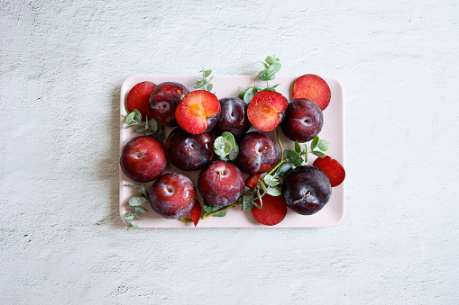 Istanbul, Turkey-August 1, 2021: Ripe angelic plums and slices in a light pink rectangular plate on a light gray rough concrete background. Shot with Canon EOS R5.