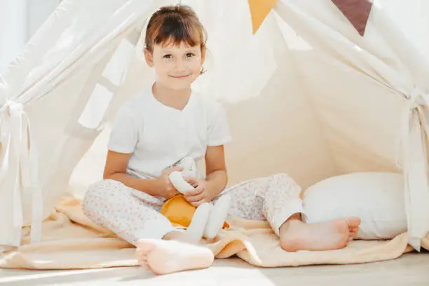 Six years cute girl playing in teepee with fabric tilda bunny at home