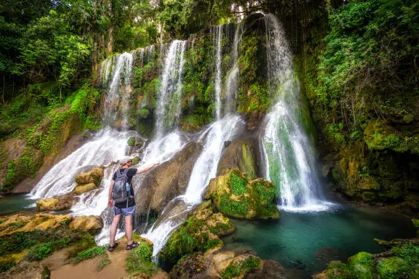 tourist in front of the big Waterfall in El Nicho, Cuba. El Nicho is located inside the Gran Parque Natural Topes de Collantes, a forested park that extends across the Sierra Escambray mountain range in central Cuba.