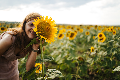 Young beautiful woman smiling and having fun in a sunflower field on a beautiful summer day. Hiding behind flowers