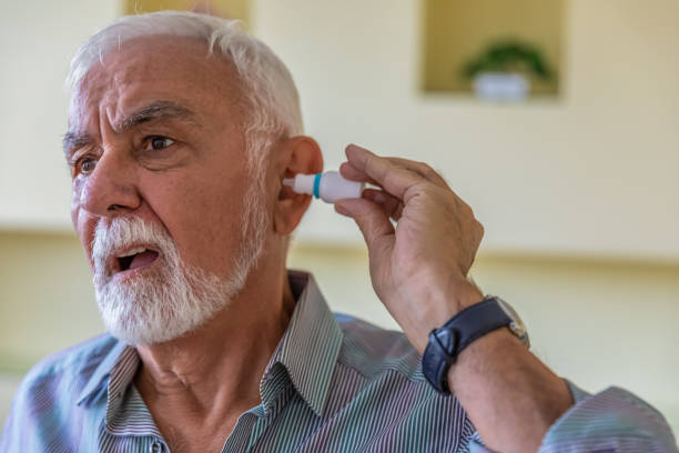 un anciano con problemas de oído está aplicando una gota para los oídos. - pain human eye senior adult men fotografías e imágenes de stock