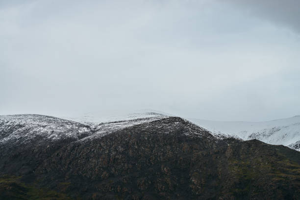 istock Minimalist highlands landscape with snow-capped mountains under cloudy sky. Snowbound high mountain range in overcast weather. Atmospheric minimalism with green mountains, white snow and gray sky. 1331856032