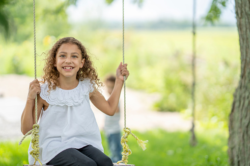 A girl smiles while swinging from a tree in a lovely rural summer setting.