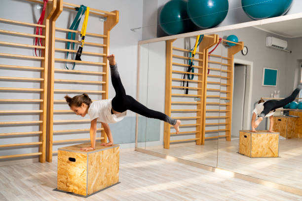 красивая маленькая девочка, занимающаяся гимнастикой, прыгает на деревян�ной коробке - floor gymnastics стоковые фото и изображения