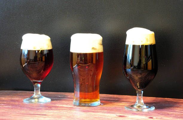 trzy szklanki z różnymi rodzajami ciemnego piwa są w rzędzie na drewnianym stole. - draught beer variation three objects zdjęcia i obrazy z banku zdjęć